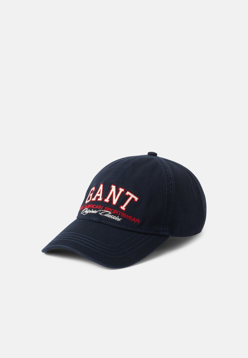 Merkin baseball cap valmistettu puuvillasta, jossa on punaisella brodeerattu "GANT"-teksti ja lisänä valkoista tekstiä, kaarevalla gladellä ja ommellulla yksityiskohdalla.