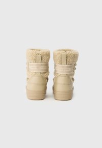 Stivaletti alla caviglia color beige in pelliccia sintetica con base in pelle liscia. Presentano un colletto imbottito, lacci regolabili e una fascia decorata con il logo.