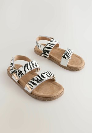 Sandali a strisce zebrate in bianco e nero con due cinturini regolabili e una soletta in suede beige, dotati di una suola in sughero testurizzata.