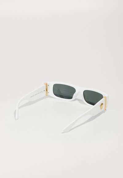 Lunettes de soleil blanches avec des verres rectangulaires, teinte gris foncé et accents dorés sur les charnières. Branches texturées avec un emblème de lion sur les côtés.