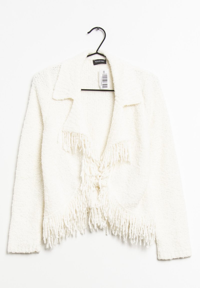 Cardigan bianco corto realizzato in un tessuto testurizzato e morbido. Presenta un colletto, frange sull'orlo e una chiusura con lacci frontali. Appeso a un gancio nero.