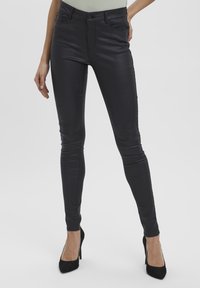 Jeans skinny en similicuir noir avec une texture lisse, taille haute, poches avant et fermeture par bouton métal. Coupe ajustée de la taille à la cheville.