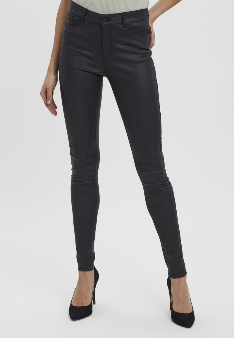 Jeans skinny en similicuir noir avec une texture lisse, taille haute, poches avant et fermeture par bouton métal. Coupe ajustée de la taille à la cheville.