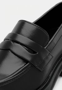 Black leather loafer featuring a smooth, shiny finish with a top strap design and stitching details along the edges. Chunky sole.