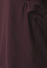 Burgundi kerge kangast topp, millel on volangkäised ja sile tekstuur. Omab pehmet langevust ja minimalistikku disaini.