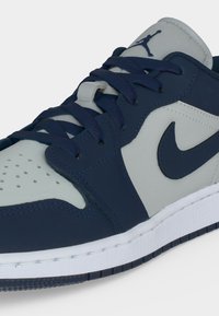 Χαμηλό sneaker με ναυτικό μπλε και ανοιχτό γκρι πάνελ, σκούρα ναυτικά κορδόνια, λογότυπο Nike Swoosh στο πλάι και λογότυπο Jumpman στη γλώσσα.