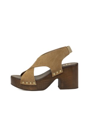 Sandalia marrón de ante con puntera abierta, tiras cruzadas, tachuelas doradas, plataforma de madera y tacón ancho con tiras traseras elásticas.