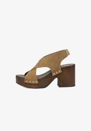 Sandalia marrón de ante con puntera abierta, tiras cruzadas, tachuelas doradas, plataforma de madera y tacón ancho con tiras traseras elásticas.