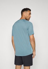 Camiseta atlética azul de manga corta, con escote redondo y paneles laterales texturizados. Combinada con pantalones cortos negros, que destacan un diseño ajustado.