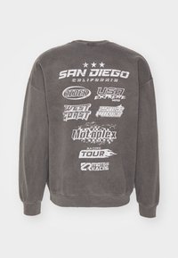 Šedá mikina s kulatým výstřihem, na zadní straně s bílým grafickým textem a logy. Mezi významné fráze patří "SAN DIEGO" a různé názvy značek.