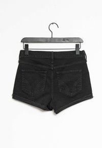 Svarta denimshorts med fransat fåll, med två bakfickor med böjda sömmar, hängande på en svart plastgalge.