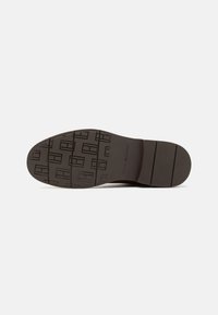 Semelle de chaussures en cuir brun avec un motif de semelle texturé, présentant des rayures horizontales et des impressions rectangulaires pour l'adhérence et la traction.