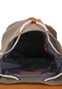 Canvas bucketväska med dragsko, beige utsida, ljusbrun mockabotten och ett mönstrat blått innerfoder. Inkluderar en zipficka.