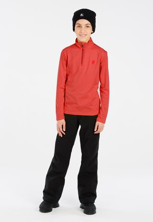 Boy wearing a red long-sleeve zip-neck shirt, black pants, black boots, and a black beanie standing against a plain white background.