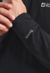 Schwarzes langärmeliges Shirt aus glattem Stoff mit einem dezenten Logo auf der Brust und dem Ärmel, das klare Linien und maßgeschneiderte Nähte präsentiert.