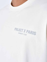 Witte katoenen t-shirt met een ronde halslijn en korte mouwen, met lichtgrijze tekst die "PROJECT X PARIS MEMBERS' CLUB" zegt.