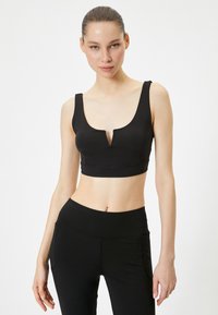 Sujeción deportiva negra con un escote en V profundo y tirantes anchos, hecha de un material elástico, cuenta con un diseño sin costuras y un ajuste ceñido.