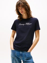 T-shirt en coton marine à manches courtes, avec logo "Tommy Hilfiger" brodé en blanc, associé à un jean de denim bleu taille haute.