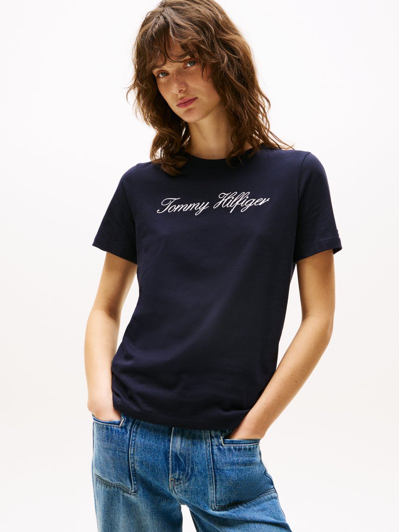 T-shirt en coton marine à manches courtes, avec logo "Tommy Hilfiger" brodé en blanc, associé à un jean de denim bleu taille haute.