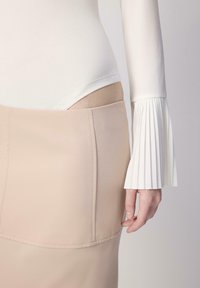 Valkoinen pitkähihainen bodysuit, jossa on poimutettu hihansuu, yhdistetty tiukkaan beigenhituiseen hameeseen. Esittelee sileää kangasta ja minimalistista muotoilua.