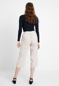Bílé pruhované kalhoty culottes s vysokým pasem a kapsami, spojené s těsným černým topem s dlouhým rukávem. Materiál se zdá být lehký a prodyšný.