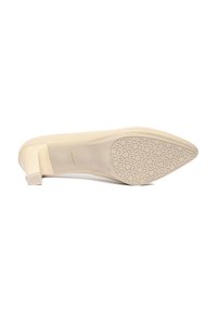 Zapato de tacón cerrado beige con tacón bajo en forma de bloque y suela de goma texturizada que presenta un patrón geométrico. Parte superior de cuero suave.