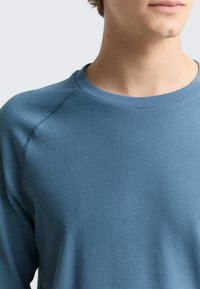 Blaues, langärmeliges Sweatshirt aus geripptem Strick mit rundem Ausschnitt und Raglanärmeln, das eine strukturierte Oberfläche und weichen Stoff bietet.