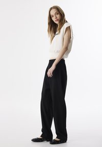 Crème cropped sweatshirt met zwarte lettering, gecombineerd met losse zwarte broek en platte zwarte schoenen met zilveren studs.