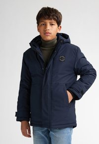 Giacca isolante di un blu navy con cappuccio, dotata di una zip frontale, due tasche laterali e una toppa con logo sul petto. Tessuto morbido e liscio.