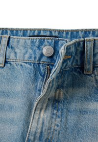 Jeans de mezclilla azul claro con una cremallera visible y cierre de botón plateado. Incluye textura desgastada y detalles de costura en contraste.