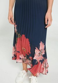 Marinblå plisserad klänning med rosa och röda blommönster vid fållen, kombinerad med vita sneakers. Mjuk tyg med en flödande design.