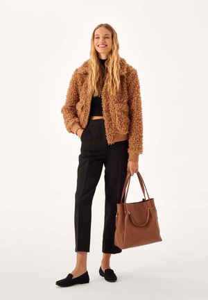 Giacca marrone pelosa con colletto, top nero corto, pantaloni neri a vita alta e borsa in pelle marrone. Mocassini neri completano il look.