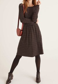 Robe noire avec un petit imprimé floral coloré, manches longues et taille froncée. Associée à des bottines marron et un sac bandoulière.