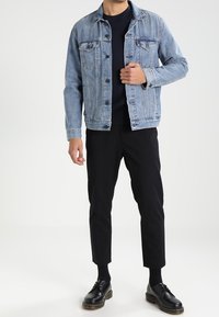 Ljusblå denimjacka med framfickor och knappstängning, i kombination med svarta tapered byxor och svarta snörskor.