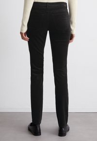 Pantalons slim-fit noirs avec une texture lisse et une taille mi-haute. Comprend des poches arrières traditionnelles et un design à jambes droites.
