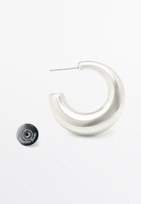 Silverfärgade metallörhängen i form av en slät, böjd design. Har en smal stift och en rund säkerhetsbackning med varumärkesdetalj.