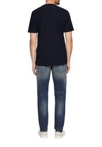 Marineblaues Baumwoll-T-Shirt mit kurzen Ärmeln und Rundhalsausschnitt, kombiniert mit hellblauen, verwaschenen Jeans und weißen Sneakers.