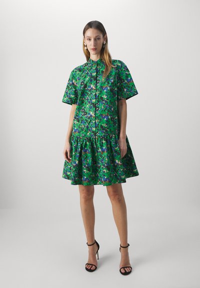 Vestito floreale verde con maniche corte, frontale con bottoni e gonna plissettata, realizzato in tessuto leggero; abbinato a tacchi strappy neri.