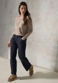 Suéter de punto marrón con escote en V y mangas largas, combinado con jeans de pierna recta azul oscuro y zapatos mocasines marrón claro.