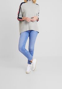 Szary sweter z wysokim kołnierzem oraz rękawami w pasiaki w kolorze granatowym, czerwonym i białym. Para z jasnoniebieskimi, obcisłymi dżinsami i białymi trampkami.