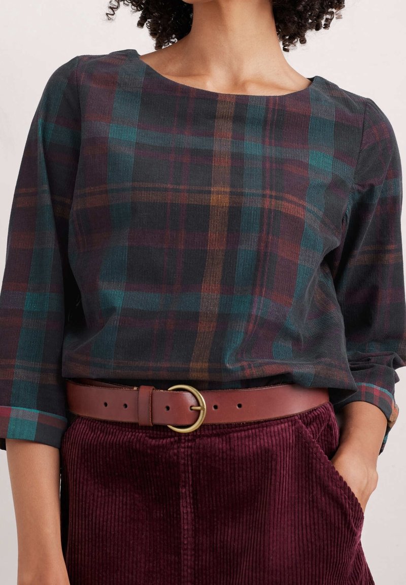 Blusa a quadri in tonalità scure con accenti in teal, mogano e oro, con scollo arrotondato e maniche a tre quarti. Indossata con una cintura marrone.