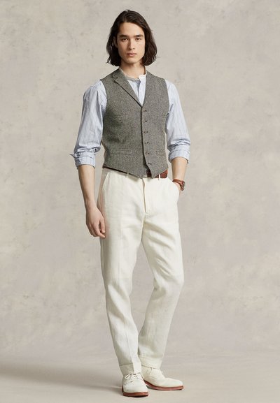 Γκρι γιλέκο σε σχέδιο χοντρού καρό με λευκό πουκάμισο με κουμπιά και παντελόνι από λινό σε κρεμ απόχρωση. Συνδυάζεται με λευκά παπούτσια που έχουν καφέ σόλες.