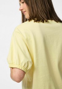 Gul bomullstopp med korta, puffiga ärmar som har elastiska manschetter. Tyget verkar mjukt, och designen är enkel och avslappnad.