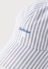 Καπέλο μπέιζμπολ με λευκές και γκρι ρίγες, με κεντημένο μπλε λογότυπο "Barbour" και μικρό έμβλημα σε σχήμα ασπίδας στο μπροστινό πάνελ.