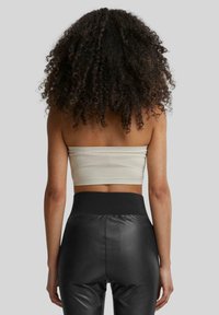 Beige ribbet crop top parret med højtaljede sorte faux læder leggings, der fremhæver en glat tekstur og tætsiddende design.