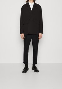 Blazer nero doppiopetto con rever a punta, abbinato a pantaloni scuri e mocassini neri. Presenta una texture liscia e una vestibilità su misura.