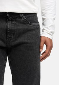 Svarte denimjeans med rett passform, med en frontlomme og subtile sømdetaljer, kombinert med en hvit langermet skjorte.