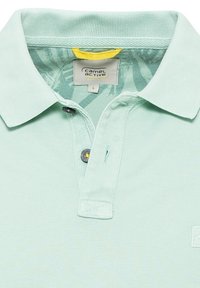 Polo shirt verde chiaro realizzato in cotone testurizzato. Presenta un colletto classico, una chiusura a due bottoni e un'etichetta con il marchio "camel active".