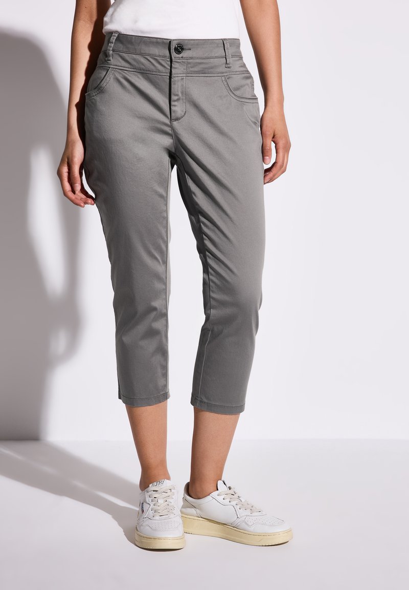 Chinos grises en tissu léger, avec une fermeture à bouton, des poches avant et un design cropped, associés à des baskets blanches.