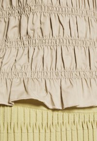 Tessuto beige, arricciato, con volant orizzontali nella parte superiore, abbinato a un tessuto verde chiaro, testurizzato e a coste nella parte inferiore.